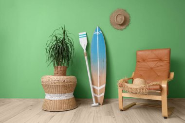 Sörf tahtası, rahat koltuk ve yeşil duvarın yanında bulunan ev bitkisi.