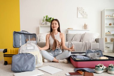 Bayan Asyalı gezgin evde bavul hazırlarken meditasyon yapıyor.