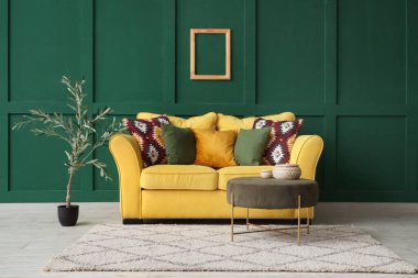 Şık oturma odasının içinde sarı kanepe, sehpa ve zeytin ağacı.