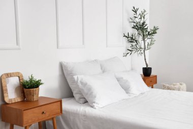 Şık bir yatak odası, rahat bir yatak odası ve komodinin üzerinde zeytin ağacı.