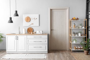 Beyaz tezgahları, kapısı, raf ünitesi ve lambası olan güzel bir mutfak.