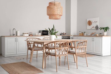 Modern mutfağın içinde beyaz tezgahlar, yemek masası, sandalyeler ve lamba var.