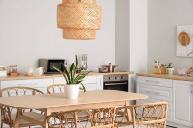 Modern mutfağın içinde beyaz tezgahlar, yemek masası, sandalyeler ve lamba var.
