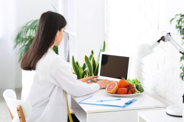 Ofiste dizüstü bilgisayarla çalışan kadın beslenme uzmanı.
