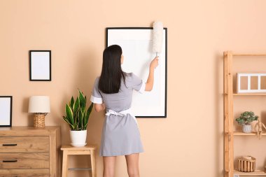 Odasında toz bezi temizleme çerçevesi olan genç oda hizmetçisi.