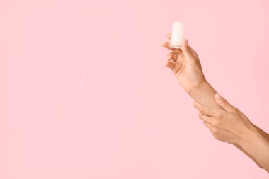 Pembe arka planda deodorantı olan kadın elleri