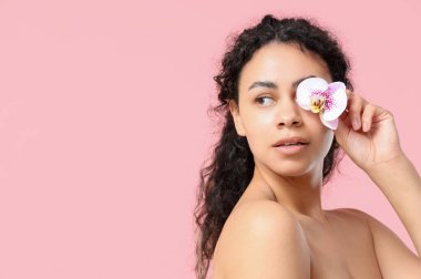 Pembe arka planda orkide çiçeğiyle güzel bir Afro-Amerikalı kadın.