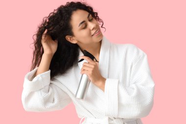 Pembe arka planda saç spreyi olan güzel, mutlu, Afro-Amerikalı bir kadın.