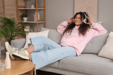Güzel, mutlu, Afro-Amerikan bir kadın kulaklıkla evde müzik dinliyor.