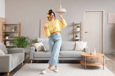 Güzel, genç, mutlu, Afro-Amerikan bir kadın kulaklıkla müzik dinliyor ve evde dans ediyor.