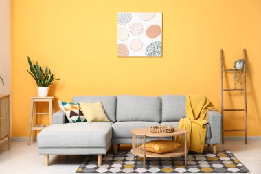 Güzel oturma odasının içinde rahat bir kanepe, çiçekler, yastıklar ve kahve masası.