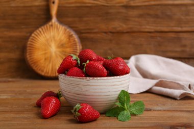 Tatlı taze çilekli kase ve ahşap arka planda nane şekeri.