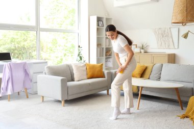 Genç bir kadın evinde topuyla bacağına masaj yapıyor.