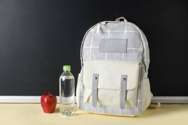 Süslü okul çantası, bir şişe su ve elma tahtaya karşı.