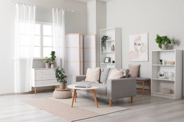 Aydınlık oturma odası, katlanır ekran, rahat kanepe, sehpa ve çekmeceler.