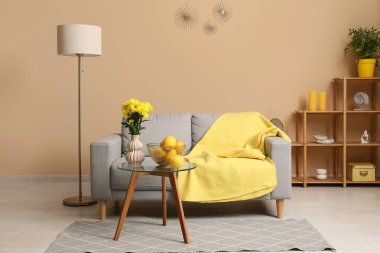 Gri kanepeli modern oturma odası, sarı çiçekli vazo ve kahve masasında portakallar.