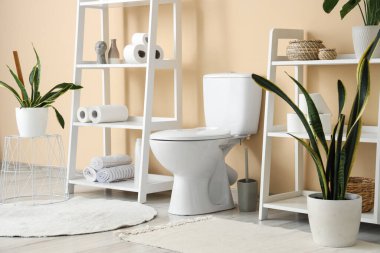 Tuvaletin içinde bej duvarın yanında klozet var.