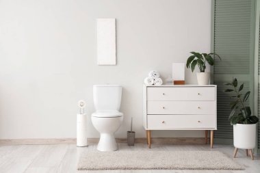 Tuvalet klozeti ve beyaz duvarın yanında çekmeceleri olan bir tuvalet.