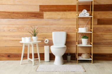 Tuvaletin içinde klozet, sehpa ve ahşap duvarın yanında raf ünitesi var.