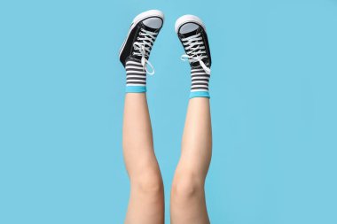 Çoraplı genç kadın bacakları ve mavi arka planda siyah spor ayakkabılar.