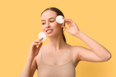 Sağlıklı cilt ve sarı arka planda pamuk pedleri olan güzel, mutlu bir kadın.