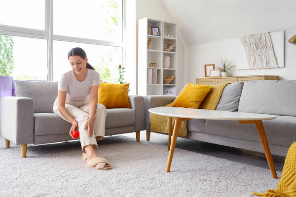 Молодая женщина массирует ногу мячом на диване дома