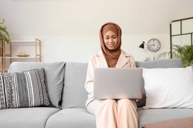 Evdeki kanepede dizüstü bilgisayarla çalışan Müslüman iş kadını.