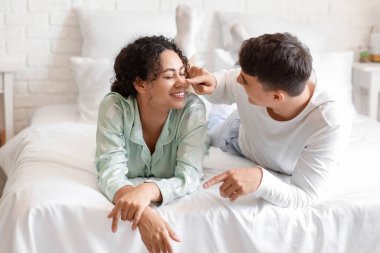 Genç adam yatak odasında kız arkadaşının burnuna dokunuyor.