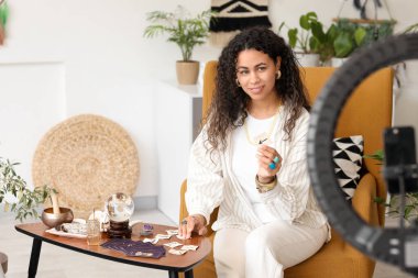 Koltuğunda rünleri olan genç Afro-Amerikan cadı evinde video kaydediyor.