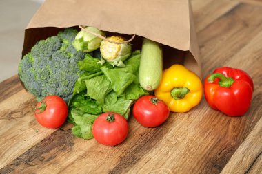 Ahşap mutfak tezgahında farklı taze sebzelerle alışveriş torbası.