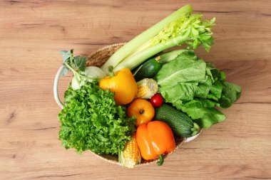 Ahşap mutfak tezgahında farklı taze sebzelerle sepet, üst manzara.