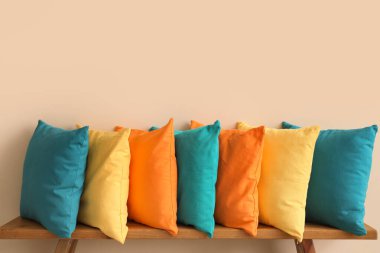 Bej duvarın yanındaki ahşap bankta renkli yastıklar