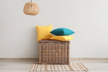 Hasır sepetin üzerinde şık yastıklar, odanın ışık duvarının yanında.