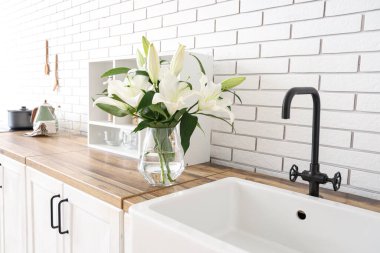 Mutfaktaki ahşap tezgahta güzel zambak çiçekleri olan vazo.