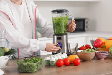 Blendırlı genç bir kadın mutfakta smoothie yapıyor, yakın plan.