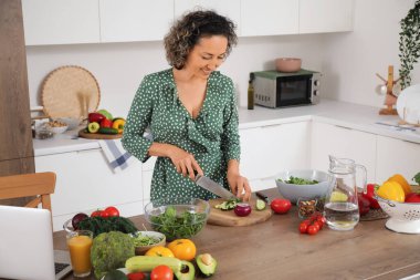 Mutfakta salatalık kesen olgun bir kadın.