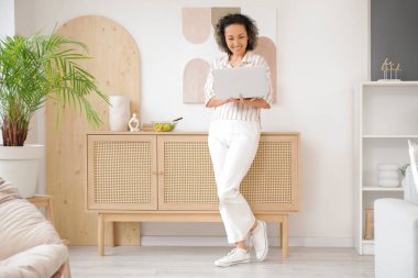 Evde dizüstü bilgisayarı ve sebze salatası olan olgun bir kadın.