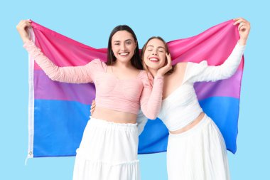 Mavi arka planda biseksüel bayrağı olan güzel bir lezbiyen çift.