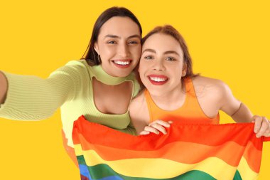 LGBT bayraklı güzel lezbiyen çift sarı arka planda selfie çekiyorlar.