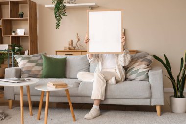 Modern oturma odasındaki gri kanepede oturan boş çerçeveli genç bir kadın.