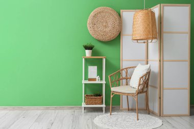 Yeşil duvarın yanında katlanır ekran, sandalye ve raf ünitesi olan bir oda.