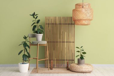 Odanın içi ahşap perdeli, sandalye ve yeşil duvarın yanındaki bitkilerle dolu.