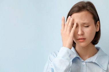 Mavi arka planda sivilce sorunu olan güzel, endişeli bir kadın.