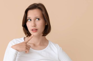 Bej arka planda sivilceleri olan düşünceli, güzel genç bir kadın.