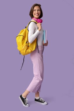 Kulaklıklı, sırt çantalı ve eflatun arkaplanlı güzel bir kız öğrenci.