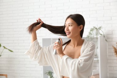 Güzel, genç, mutlu bir kadın evde saç spreyi sıkıyor.