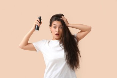Bej arka planda saç spreyi ile şok olmuş güzel bir genç kadın.