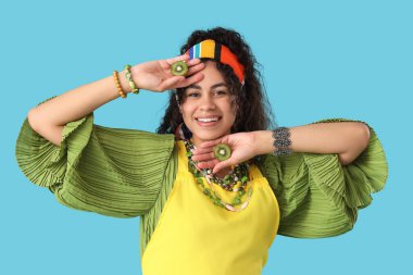 Mavi arka planda bir dilim kivi olan güzel, mutlu, Afro-Amerikalı bir kadın.