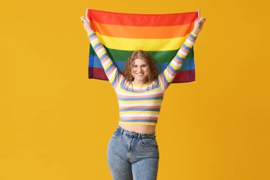 Sarı arka planda LGBT bayrağı olan mutlu genç bir kadın.