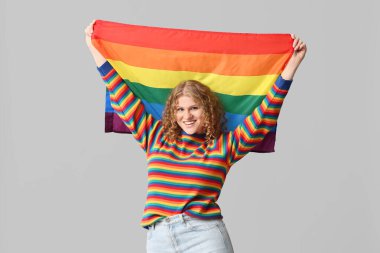 Gri arka planda LGBT bayrağı olan mutlu genç bir kadın.